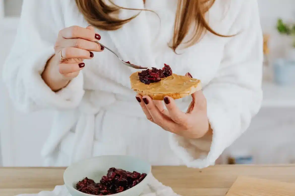Cuillère de beurre de cacahuètes crémeux sur une tranche de pain complet, accompagnée d'amandes et de dattes