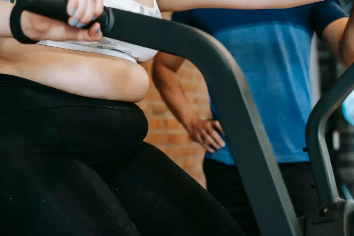 Personne en mouvement sur un vélo elliptique dans un espace fitness lumineux, mains sur les poignées, posture engagée.