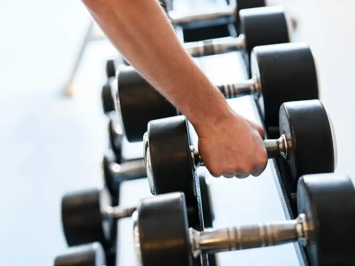 Mains ajustant des poids sur une cage de squat près d'une fenêtre, carnet d'entraînement visible